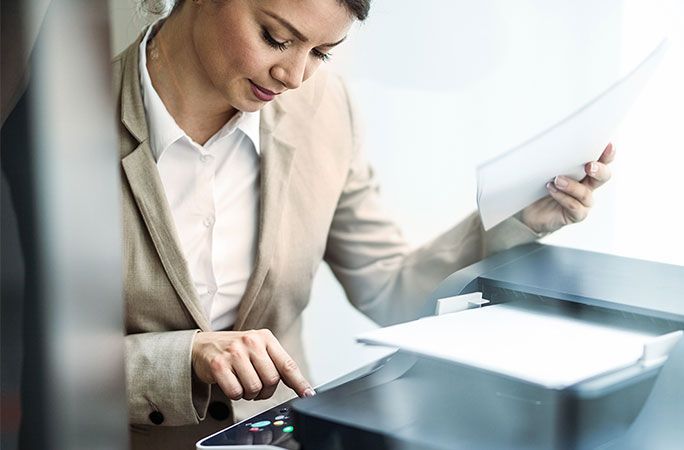 Young businesswoman pressing start button on fax machine. The view is through glass.